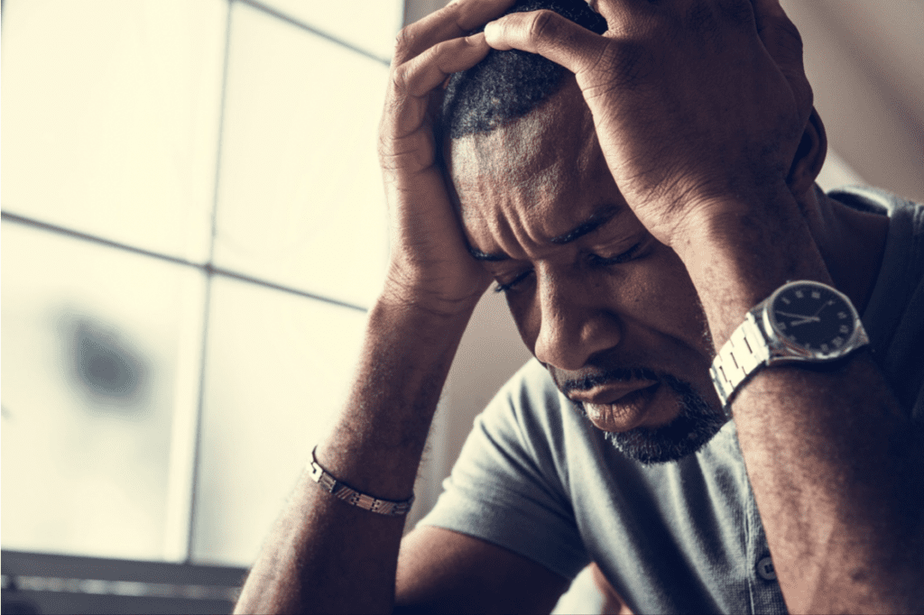 A man holding his head in his hands with his eyes closed, looking stressed and though he is experiencing a headache.